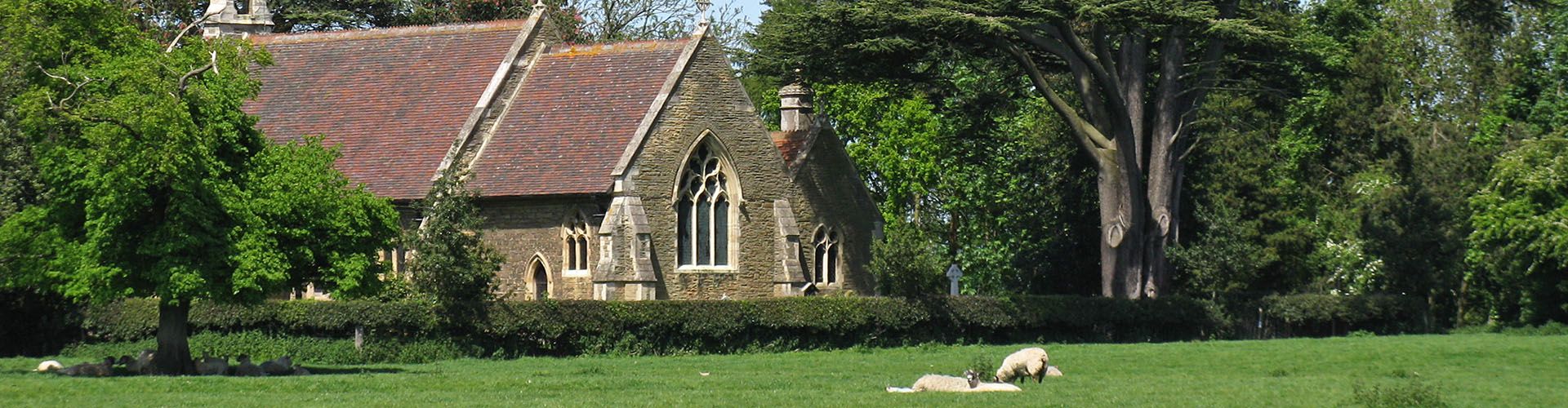 A view of a church with a green field containing sheep in the foreground.