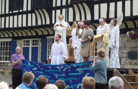 Amateur actors perform a play in front of an historic timber-framed building.