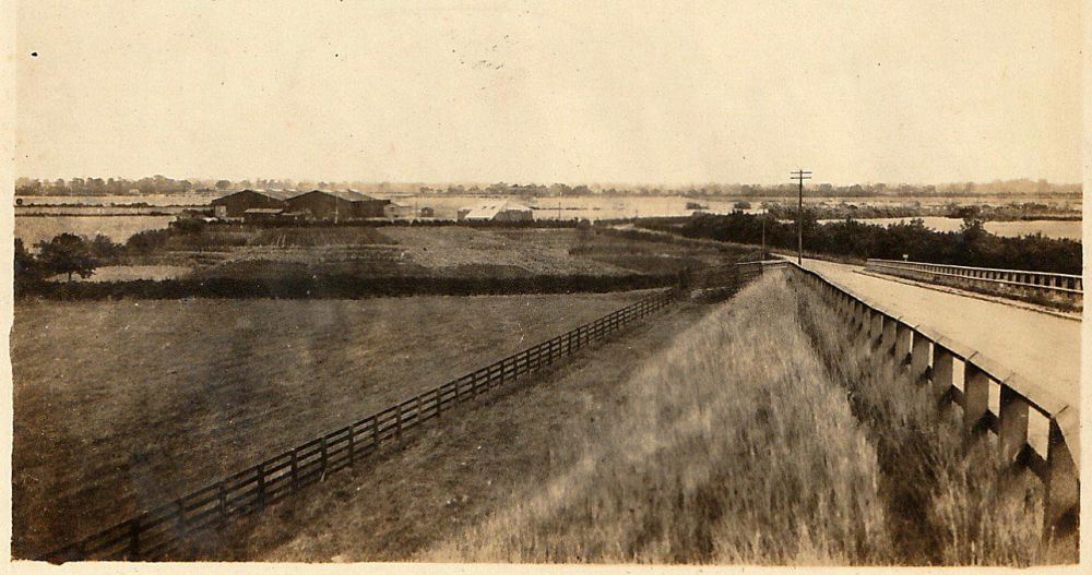 A sepia-tinged photograph of fence-lined fields and a road.
